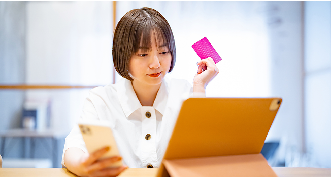 タブレットを見ながらスマホとクレジットカードを持つ女性